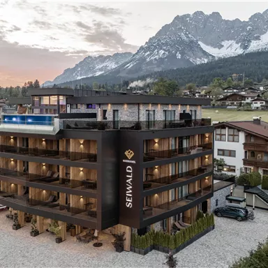 Ein modernes Hotel in den Bergen mit einer malerischen Umgebung. Die Landschaft wird von schneebedeckten Gipfeln und typischer alpenländischer Architektur geprägt.