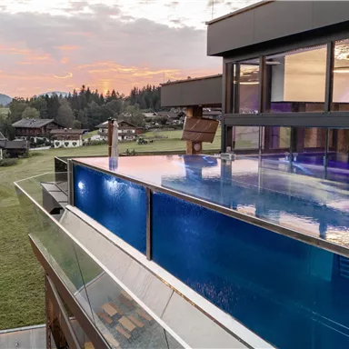 Ein modernes Haus mit einem Infinity-Pool und großen Fenstern. Im Hintergrund sind Berge und eine wunderschöne Landschaft zu sehen.
