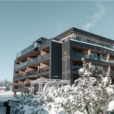 Ein modernes Gebäude im winterlichen Schnee. Die Fassade besteht aus Holz und bietet Balkone mit Aussicht.