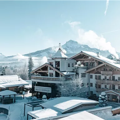 Ein malerisches Chalet inmitten einer verschneiten Winterlandschaft. Die Sonne scheint und der Himmel ist klar.