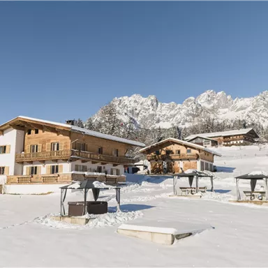 A picturesque winter landscape with snow-covered hills and traditional wooden houses. The clear blue sky complements the serene atmosphere.