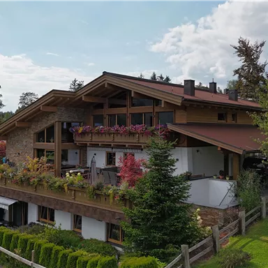 Ein schönes Haus im alpinen Stil mit einem großen Balkon. Umgeben von grünen Wiesen und Bäumen.
