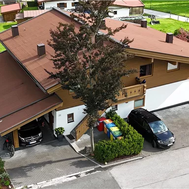 Ein großes, zweigeschossiges Haus mit einem braunen Dach und grünen Rasenflächen. Parkplätze sind direkt vor dem Haus vorhanden.