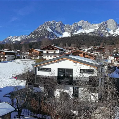 Ein schneebedecktes Dorf umgeben von majestätischen Bergen. Der klare blaue Himmel sorgt für eine entspannte Winteratmosphäre.