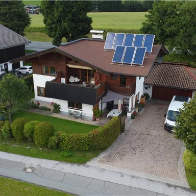 Ein modernes "Tiroler Niedrigenergiehaus" mit Solarpanelen auf dem Dach und Photovoltaikanlagen am Balkon. Der Garten ist gepflegt und das Umfeld ist grün.