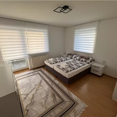 A bright bedroom with two beds and a modern rug. Large windows let in plenty of light and create an inviting atmosphere.