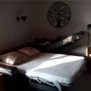 Ein gemütliches Schlafzimmer mit einem Bett, auf dem sich ein Kissen liegt. Es gibt einen bequemen Sessel und eine kleine Stehlampe, die eine warmen Atmosphäre schaffen.
