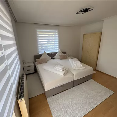 Ein modernes Schlafzimmer mit einem Doppelbett und weißen Bettwäschen. Große Fenster sorgen für viel Tageslicht und eine helle, freundliche Atmosphäre.