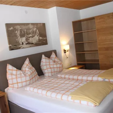 Ein gemütliches Schlafzimmer mit einem Doppelbett und modernen Holzdetails. Im Hintergrund ist ein großes Regal zu sehen.