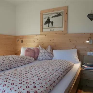 Ein gemütliches Schlafzimmer mit einem Doppelbett und vielen Kissen. Die Wände sind aus Holz und es gibt dekorative Bilder sowie Nachttischlampen.