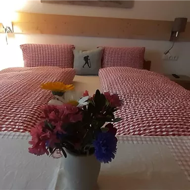 Ein gemütliches Zimmer mit zwei Einzelbetten und karierten Bettbezügen. Auf dem Tisch steht ein kleines Blumenarrangement.
