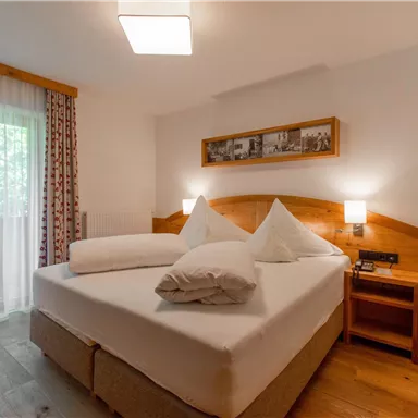 Ein gemütliches Schlafzimmer mit einem großen Doppelbett und zwei Kopfkissen. Große Fenster sorgen für viel Tageslicht.