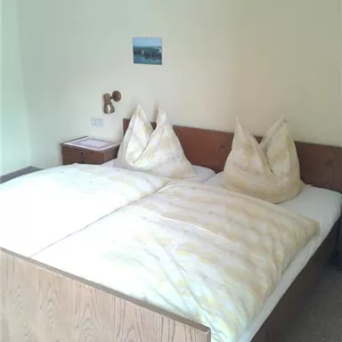 A cozy bedroom with a large double bed and two decorative pillows. A small picture hangs on the wall, and there is a nightstand next to the bed.