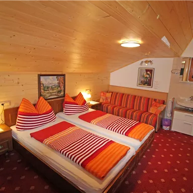 Ein gemütliches Schlafzimmer mit zwei Betten und orangefarbenen Kissen. Die Wände sind aus Holz, und es gibt eine Sitzgelegenheit sowie ein Badezimmer.