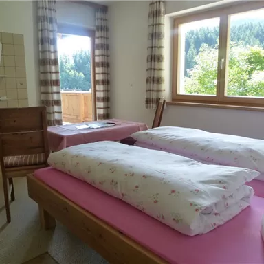 Ein einfaches Zimmer mit zwei Betten und einem Stuhl. Der Raum hat ein Fenster mit Blick auf die grüne Landschaft draußen.