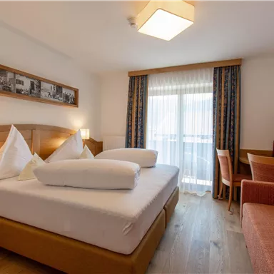 Ein gemütliches Hotelzimmer mit einem großen Bett, einem Schreibtisch und einer Sitzecke. Große Fenster lassen viel Licht herein und bieten einen Blick nach draußen.