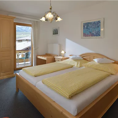 Ein helles Schlafzimmer mit einem großen Doppelbett und gelben Bettdecken. Es gibt einen Balkon mit Blick auf die Berglandschaft und eine gemütliche Holz-Ausstattung.