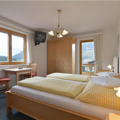 Ein gemütliches Schlafzimmer mit zwei Betten und gelben Bettdecken. Der Raum hat große Fenster mit Blick auf die Berge und ist freundlich eingerichtet.
