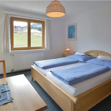 Ein gemütliches Schlafzimmer mit zwei Einzelbetten und hellen Holzmöbeln. Große Fenster bieten einen Blick auf die Landschaft.
