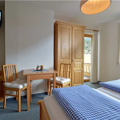 Ein gemütliches Schlafzimmer mit zwei Einzelbetten, einem Tisch und Stühlen. Große Fenster sorgen für viel Tageslicht und bieten einen Blick auf die Umgebung.