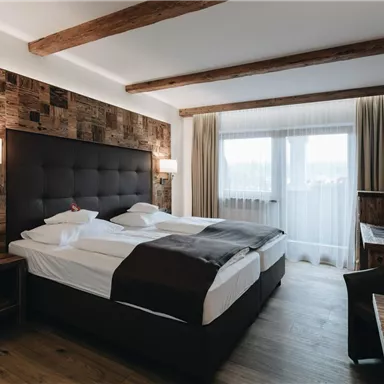 Ein modernes Hotelzimmer mit einem großen Doppelbett und Holzelementen. Lichtdurchflutete Fenster sorgen für eine freundliche Atmosphäre.