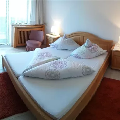 A cozy bedroom with a large double bed and light wood. The windows let in plenty of light and create an inviting atmosphere.