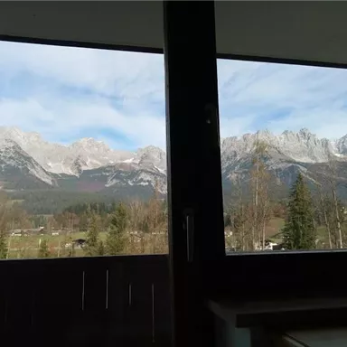 An impressive mountain landscape with snow-capped peaks and a clear sky. In the foreground, trees and meadows can be seen.