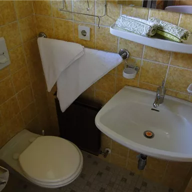 A small bathroom with yellow tiles. There is a toilet and a sink, as well as a towel and toiletries.