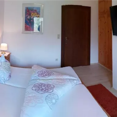 A cozy bedroom with two beds, a television, and modern amenities. The room is bright and inviting, with a bathroom in the background.