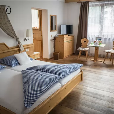 Ein gemütliches Zimmer mit einem großen Bett und Holzmöbeln. Es gibt einen Tisch mit Stühlen und viel natürliches Licht durch die Fenster.