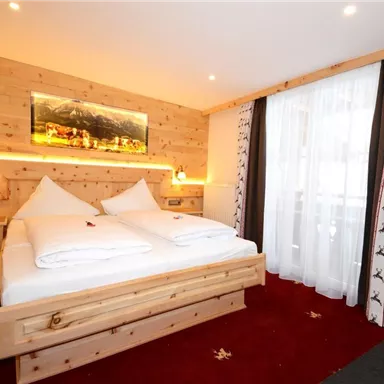 Ein gemütliches Zimmer mit einem Doppelbett und Holzverkleidung. Helle Fenster sorgen für eine freundliche Atmosphäre.