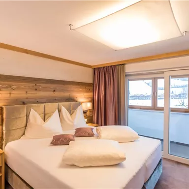 Ein gemütliches Schlafzimmer mit einem großen Bett und modernen Möbeln. Große Fenster bieten einen Blick auf die verschneite Landschaft.