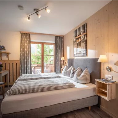 Ein gemütliches Schlafzimmer mit einem Doppelbett und modischer Dekoration. Große Fenster sorgen für viel Tageslicht und einen Blick nach draußen.