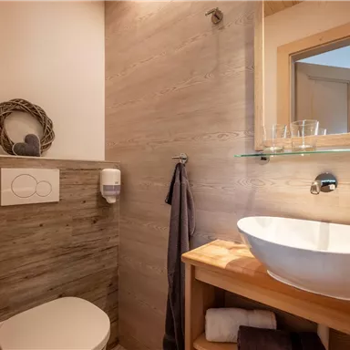 Ein modernes Badezimmer mit Holzwänden und eleganten Sanitäranlagen. Das Waschbecken ist auf einem Holzregal platziert und ein großes Fenster sorgt für natürliches Licht.