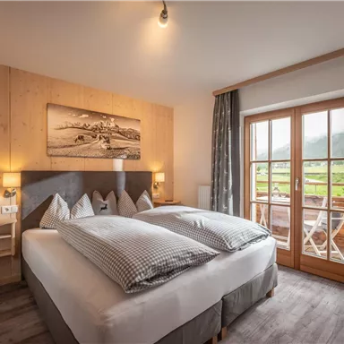 Ein gemütliches Schlafzimmer mit zwei Betten und modernen Möbeln. Große Fenster bieten einen Blick auf die Natur draußen.