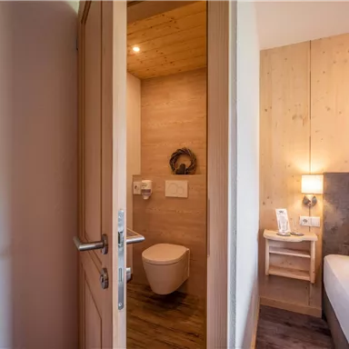 Ein stilvolles Zimmer mit einem modernen Bad und einem gemütlichen Bett. Die Holzverkleidung schafft eine warme Atmosphäre.