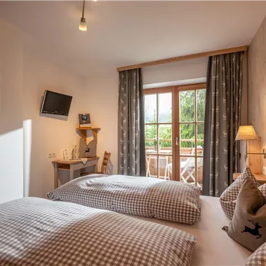 Ein gemütliches Hotelzimmer mit zwei Einzelbetten und einem modernen Interieur. Große Fenster sorgen für viel Tageslicht und bieten einen Blick auf den Balkon.
