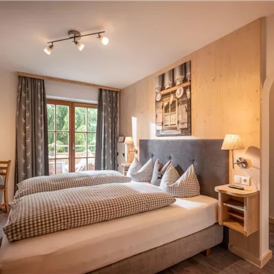 Ein gemütliches Schlafzimmer mit zwei Betten, Holzdetails und modernen Möbeln. Große Fenster sorgen für viel natürliches Licht.