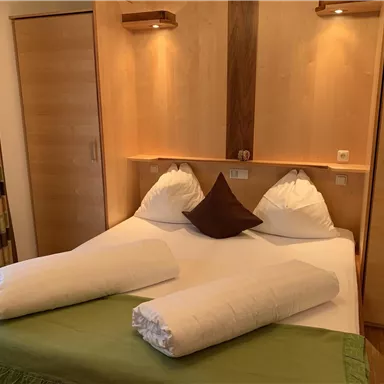 Ein gemütliches Schlafzimmer mit einem Doppelbett und weichen Kissen. Die Holzmöbel sorgen für eine warme Atmosphäre.