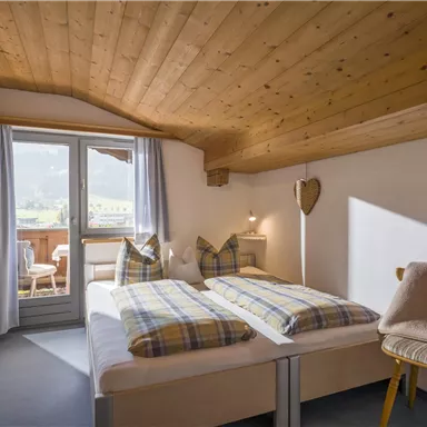 A cozy bedroom with a double bed and wooden ceiling. View of the balcony with a glimpse of the surrounding landscape.