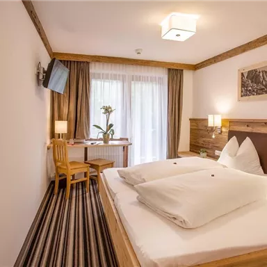 A cozy hotel room with two beds, a table, and chairs. Large windows let in plenty of light and offer a view of nature.