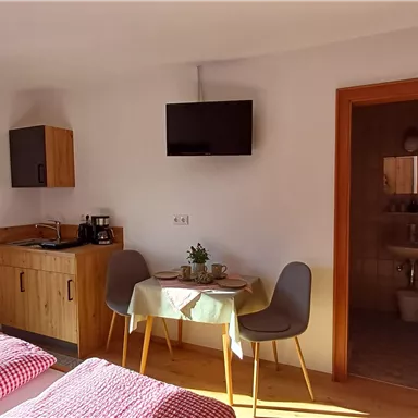 Ein gemütliches Zimmer mit zwei Betten, einem Esstisch und einem Fernseher. Die Einrichtung ist hell und modern, mit Zugang zu einem Badezimmer.