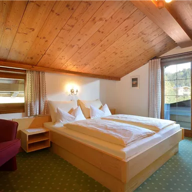 Ein gemütliches Schlafzimmer mit einem Doppelbett und einer Holzdecke. Der Raum verfügt über große Fenster mit Aussicht und einen kleinen Sitzbereich.