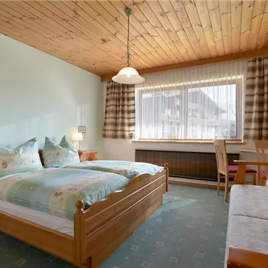 A cozy bedroom with wooden ceilings and large windows. The room is furnished with a double bed, a seating area, and warm colors.