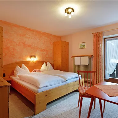 Ein gemütliches Schlafzimmer mit zwei Betten und Holzmöbeln. Das Zimmer hat einen sonnigen Balkon und eine freundliche, entspannte Atmosphäre.