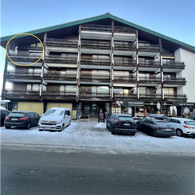 Ein modernes Wohngebäude mit mehreren Etagen und Balkonen. Vor dem Gebäude parken Autos auf einer schneebedeckten Straße.