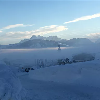 Eine verschneite Landschaft mit Bergen im Hintergrund und einem nebligen Himmel. Die Uferlinie ist von Schnee bedeckt und es ist sehr ruhig.