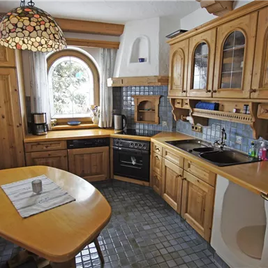 Eine gemütliche Küche mit Holzschränken und einem runden Essbereich. Das Fenster bietet einen schönen Ausblick und die Beleuchtung ist warm und einladend.