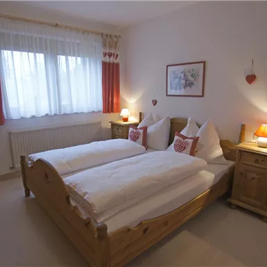 Ein gemütliches Schlafzimmer mit zwei Einzelbetten und Holzmöbeln. Die Fenster sind mit hellen Vorhängen dekoriert, und eine warme Lampe sorgt für eine einladende Atmosphäre.