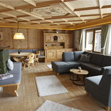 Ein gemütlicher Wohnraum mit Holzmöbeln und einem eleganten Deckenpaneel. Große Fenster sorgen für viel Tageslicht und eine einladende Atmosphäre.